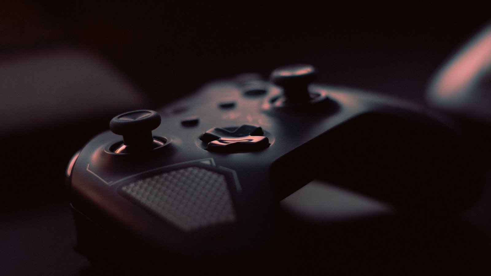 Controle de videogame escuro visto de perto, com os botões e as alavancas iluminados por uma luz fraca