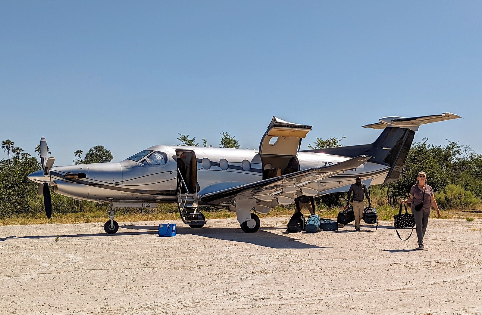 Avião Pilatus PC-12 numa pista de terra no delta do Okavango, em Botsuana, com a porta aberta e bagagens ao lado